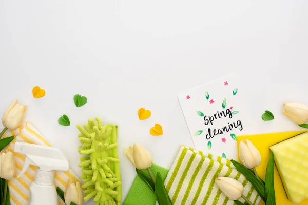 Top view of spring tulips, green and yellow cleaning supplies with hearts near spring cleaning card on white background — Stock Photo
