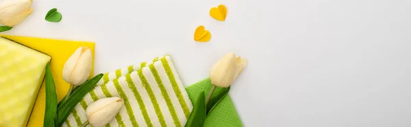 Top view of spring tulips, green and yellow cleaning supplies with hearts on white background, panoramic shot — Stock Photo