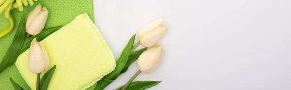 Top view of spring tulips and green cleaning supplies on white background, panoramic shot — Stock Photo