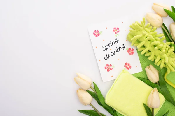 Vista superior de tulipas de primavera e suprimentos de limpeza verde perto de cartão de limpeza de primavera no fundo branco — Fotografia de Stock