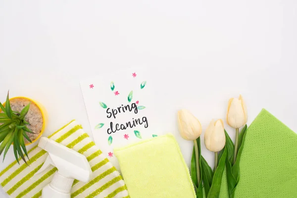 Vista superior de tulipas de primavera e planta verde perto de suprimentos de limpeza e cartão de limpeza de primavera no fundo branco — Fotografia de Stock