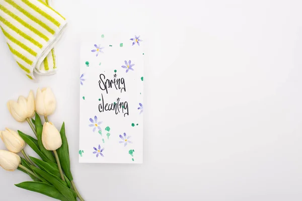 Vue de dessus des tulipes et serviettes de printemps près de la carte de nettoyage de printemps sur fond blanc — Photo de stock