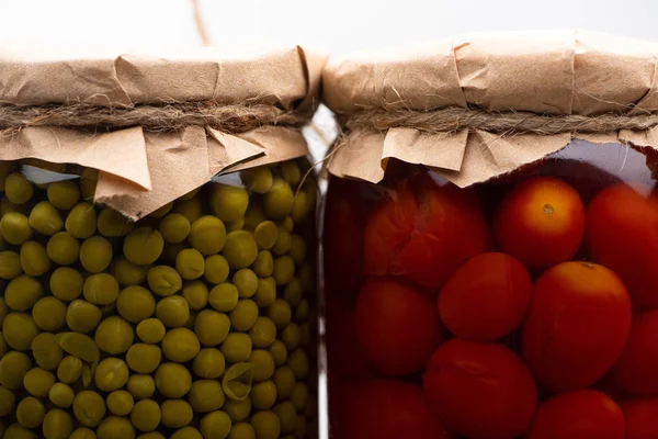 Vista de cerca de tomates enlatados sabrosos caseros y guisantes verdes en frascos - foto de stock