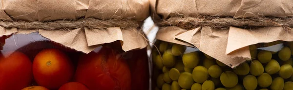 Close up view of homemade tasty canned tomatoes and green peas in jars, panoramic shot — Stock Photo