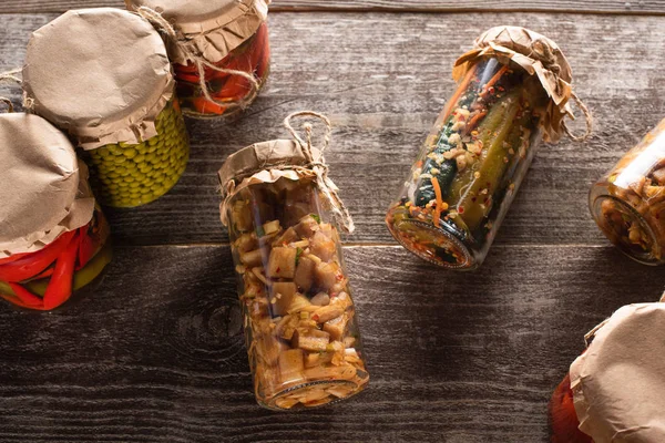 Blick von oben auf hausgemachte leckere Essiggurken in Gläsern auf Holztisch — Stockfoto