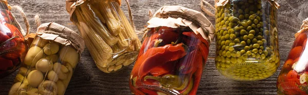 Top view of homemade delicious pickles in jars on wooden table, panoramic shot — Stock Photo