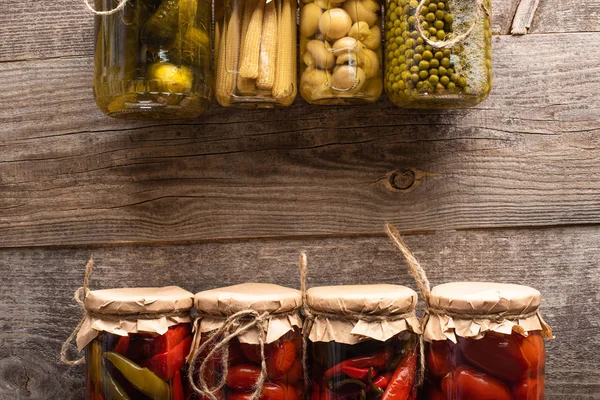 Vista superior de verde y rojo sabrosos encurtidos caseros en frascos en mesa rústica de madera - foto de stock