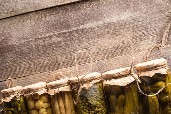 Vista superior de verdes sabrosos encurtidos caseros en frascos en mesa rústica de madera - foto de stock