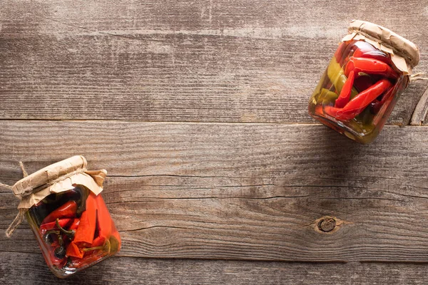 Vista superior de rojo casero sabrosos chiles en vinagre en frascos en mesa de madera - foto de stock