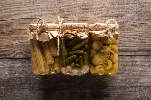 Vista dall'alto di deliziosi cetrioli fatti in casa gustosi sottaceti, mais e funghi su tavolo rustico in legno — Foto stock