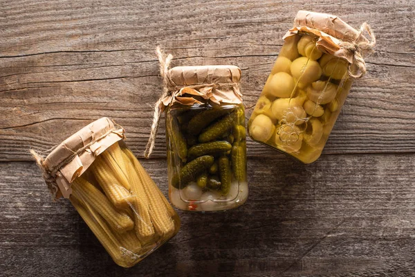 Blick von oben auf köstliche hausgemachte schmackhafte eingelegte Gurken, Mais und Pilze auf rustikalem Holztisch — Stockfoto