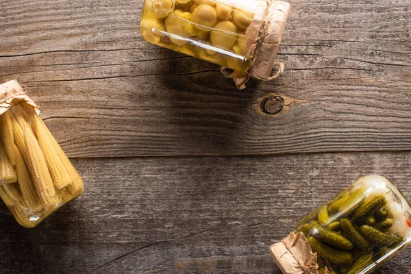 Blick von oben auf köstliche hausgemachte schmackhafte eingelegte Gurken, Mais und Pilze auf rustikalem Holztisch — Stockfoto