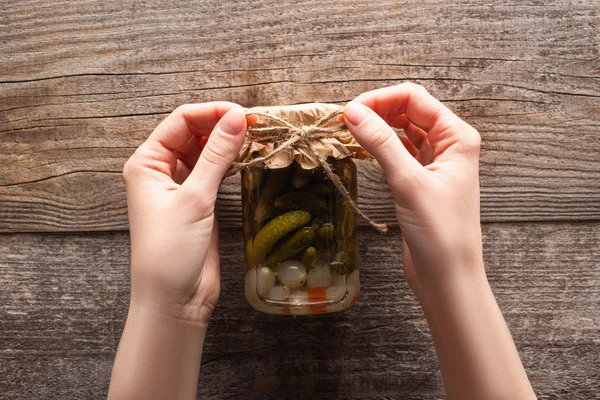 Cropped view of woman holding bow on homemade tasty canned cucumbers in jar on wooden table — Stock Photo