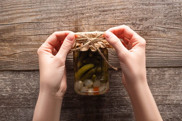 Abgeschnittene Ansicht einer Frau mit Schleife auf hausgemachten schmackhaften Gurkenkonserven im Glas auf dem Holztisch — Stockfoto