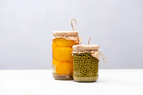 Hausgemachte köstliche eingelegte gelbe Tomaten und grüne Erbsen in Gläsern isoliert auf grau — Stockfoto