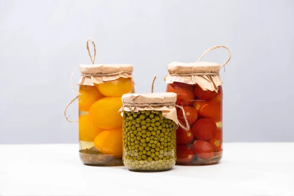 Homemade delicious pickled tomatoes and green peas in jars isolated on grey — Stock Photo