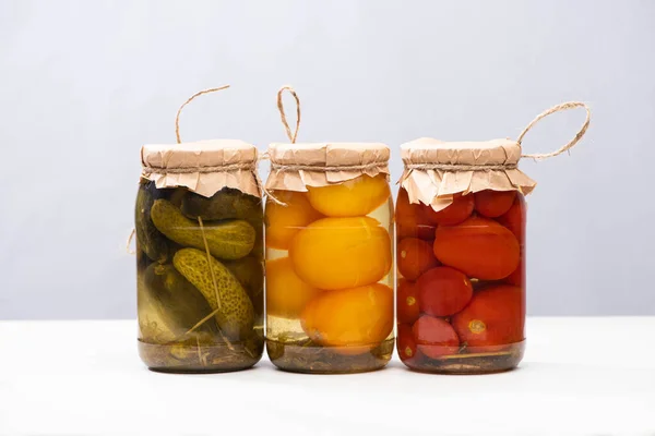 Hausgemachte köstliche eingelegte Tomaten und Gurken in Gläsern isoliert auf grau — Stockfoto