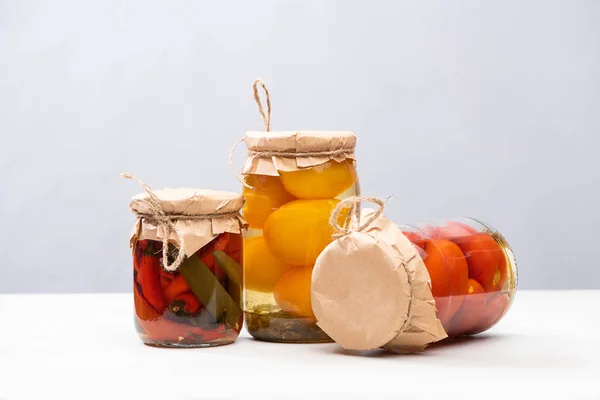 Hausgemachte köstliche eingelegte Tomaten und Chilischoten in Gläsern isoliert auf grau — Stockfoto