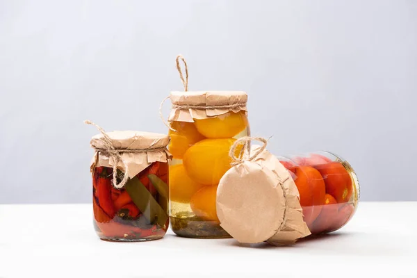 Homemade delicious pickled tomatoes and chili peppers in jars isolated on grey — Stock Photo