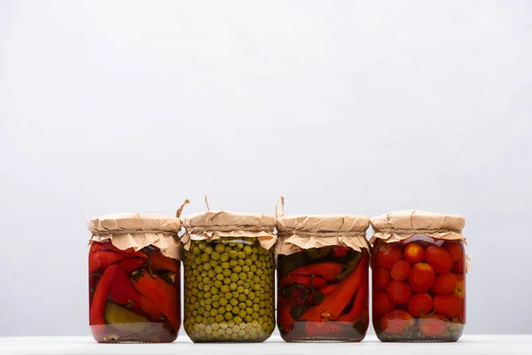 Délicieuses tomates marinées maison, piments et pois verts dans des pots isolés sur gris — Photo de stock