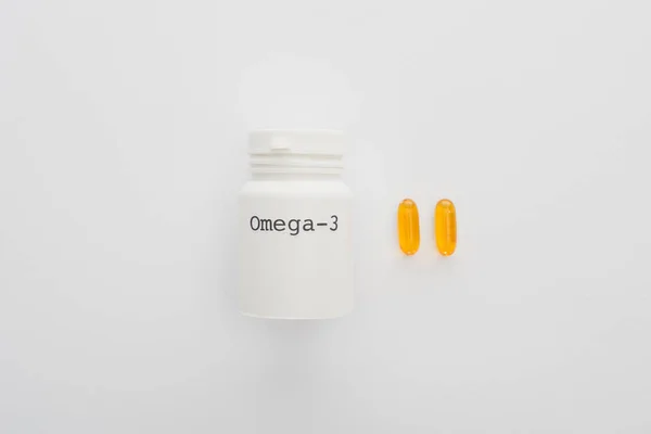 Vista dall'alto del contenitore con scritte omega-3 e capsule gialle su sfondo bianco — Foto stock