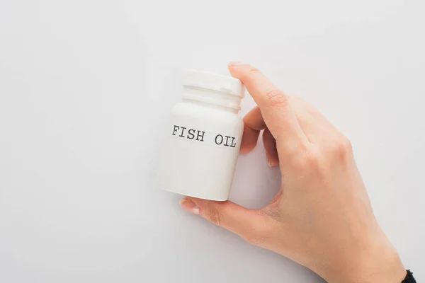 Vista ritagliata di donna che tiene contenitore con olio di pesce lettering su sfondo bianco — Foto stock