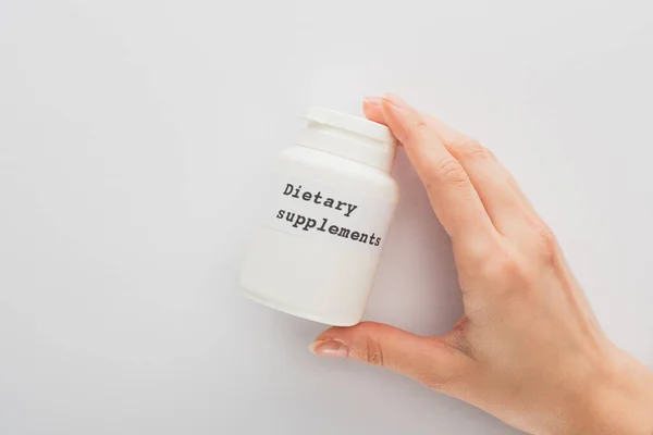 Vista cortada de mulher segurando recipiente com suplementos dietéticos lettering no fundo branco — Fotografia de Stock