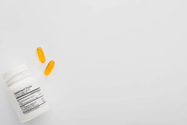 Top view of container and fish oil capsules on white background — Stock Photo