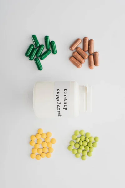 Top view of container with dietary supplements lettering with pills and capsules on white background — Stock Photo