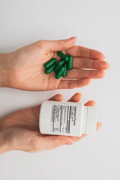 Cropped view of woman holding container and green capsules on white background — Stock Photo