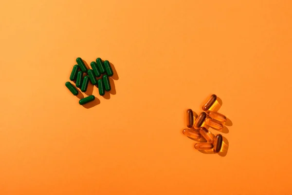 Top view of brown and green capsules on orange — Stock Photo