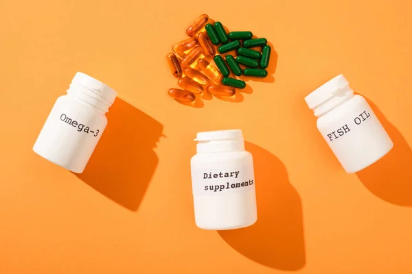 Top view of containers with omega-3, fish oil and dietary supplements lettering with capsules on orange — Stock Photo