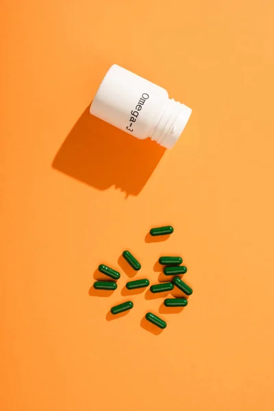 Top view of container with omega-3 lettering and green capsules on orange background — Stock Photo