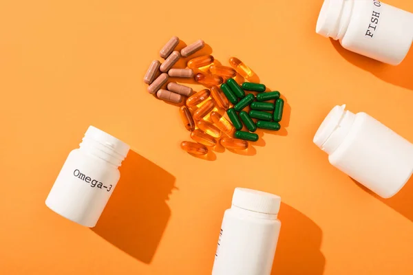 Top view of containers with omega-3 and fish oil lettering near capsules on orange background — Stock Photo