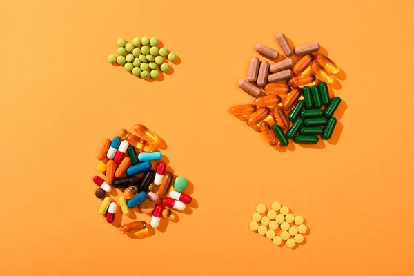 Draufsicht auf bunte Pillen und Kapseln auf orangefarbenem Hintergrund — Stockfoto