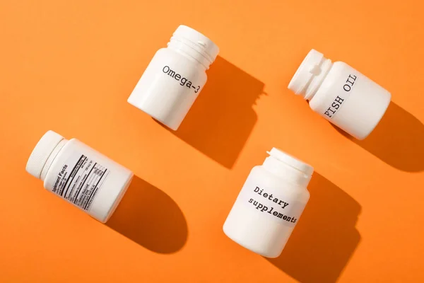 Flat lay com recipientes com ômega-3, óleo de peixe e suplementos dietéticos lettering em fundo laranja — Fotografia de Stock