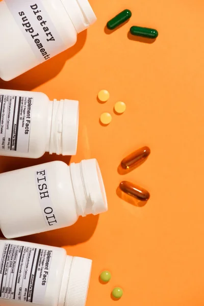 Visão superior de recipientes com óleo de peixe e suplementos dietéticos lettering perto de pílulas em fundo laranja — Fotografia de Stock