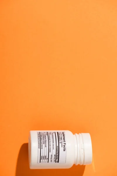 Vista superior do recipiente branco com suplementos dietéticos sobre fundo laranja — Fotografia de Stock