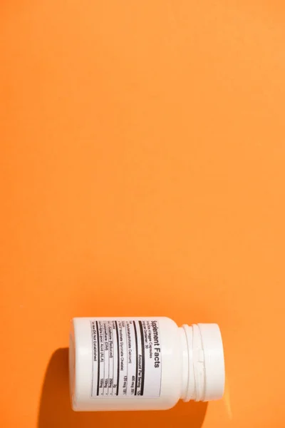 Top view of white container with dietary supplements on orange background — Stock Photo