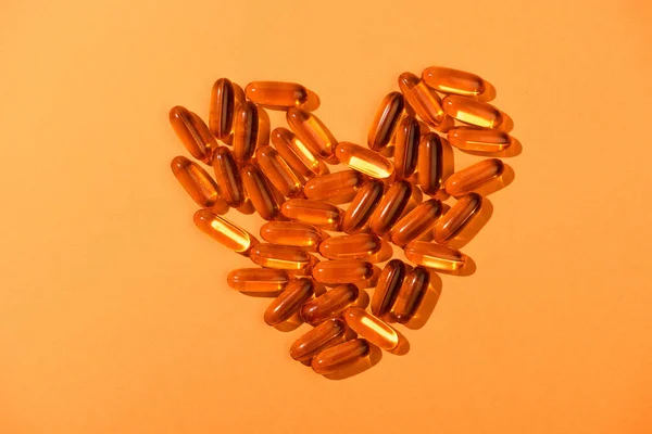 Top view of decorative heart from fish oil capsules on orange background — Stock Photo