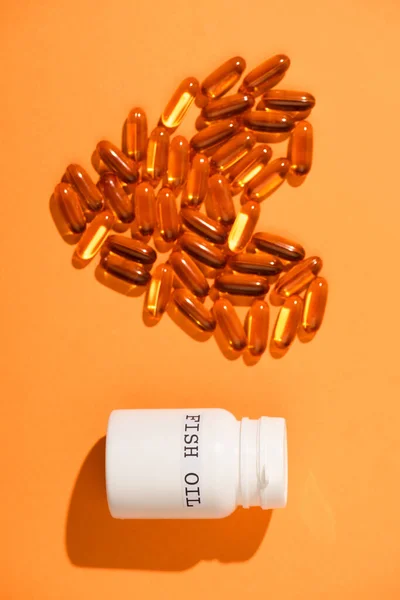 Top view of decorative heart from capsules and container with fish oil lettering on orange background — Stock Photo