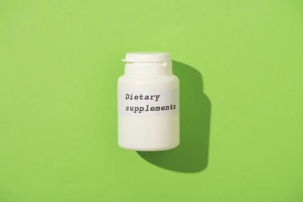 Visão superior do recipiente com suplementos dietéticos lettering em fundo verde — Fotografia de Stock