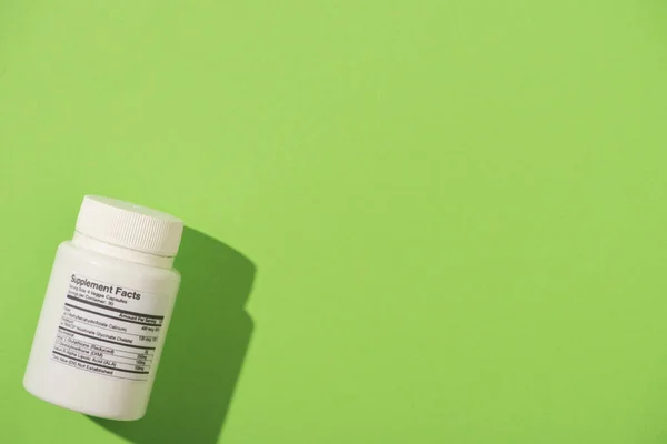 Draufsicht auf weißen Behälter mit Nahrungsergänzungsmitteln auf grünem Hintergrund — Stockfoto