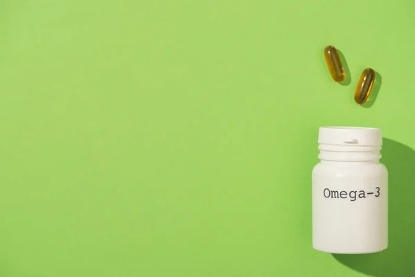 Top view of container with omega-3 lettering near capsules on green — Stock Photo