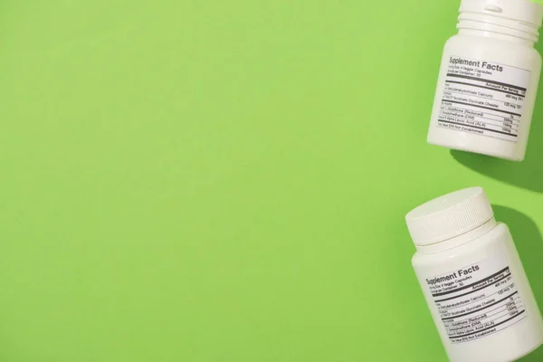 Top view of containers with dietary supplements on green background — Stock Photo