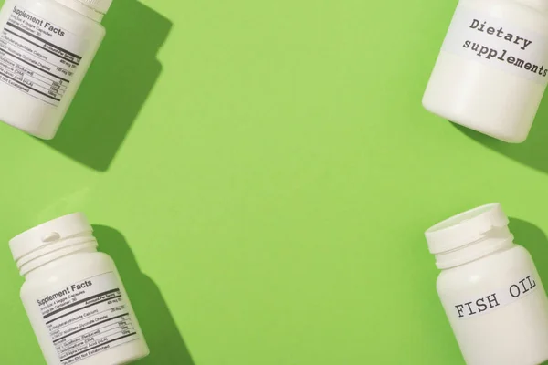 Top view of containers with fish oil and dietary supplements lettering on green background — Stock Photo