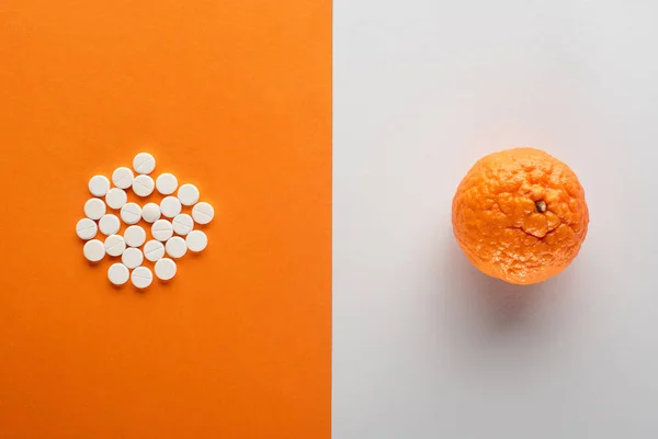 Top view of pills and mandarin on white and orange background — Stock Photo