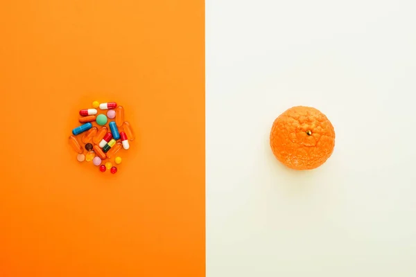 Top view of colorful pills and mandarin on white and orange background — Stock Photo