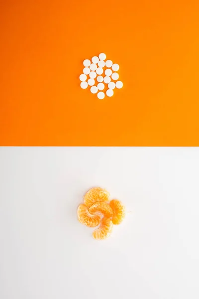 Vista superior de píldoras y mandarina sobre fondo blanco y naranja - foto de stock