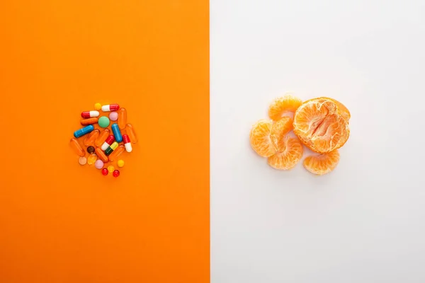 Vue du dessus des médicaments colorés et de la mandarine sur fond blanc et orange — Photo de stock